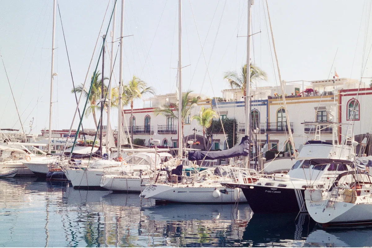 Veleros amarrados en el puerto de Mogán frente a casas blancas con palmeras