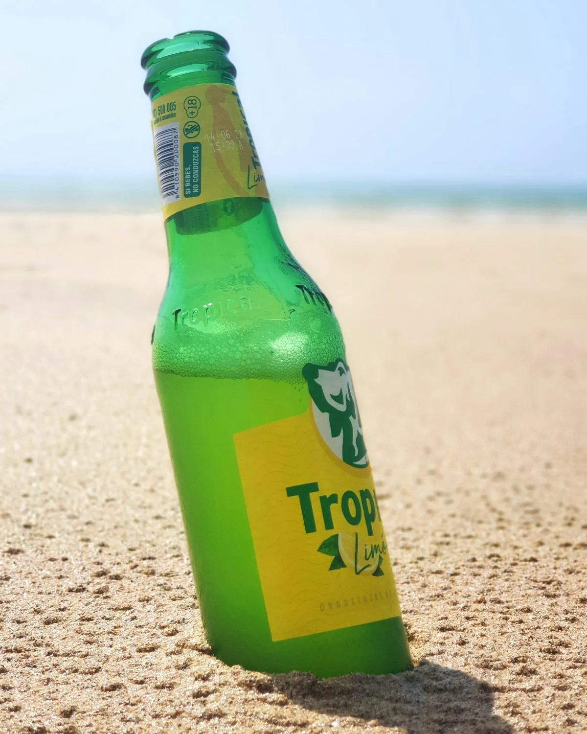 Botellín de cerveza Tropical clavado en la arena de una playa