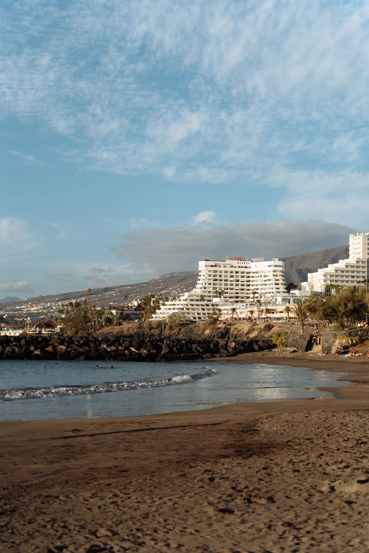 Playa de San Agustín con un espigón de rocas y hoteles blancos escalonados en la ladera