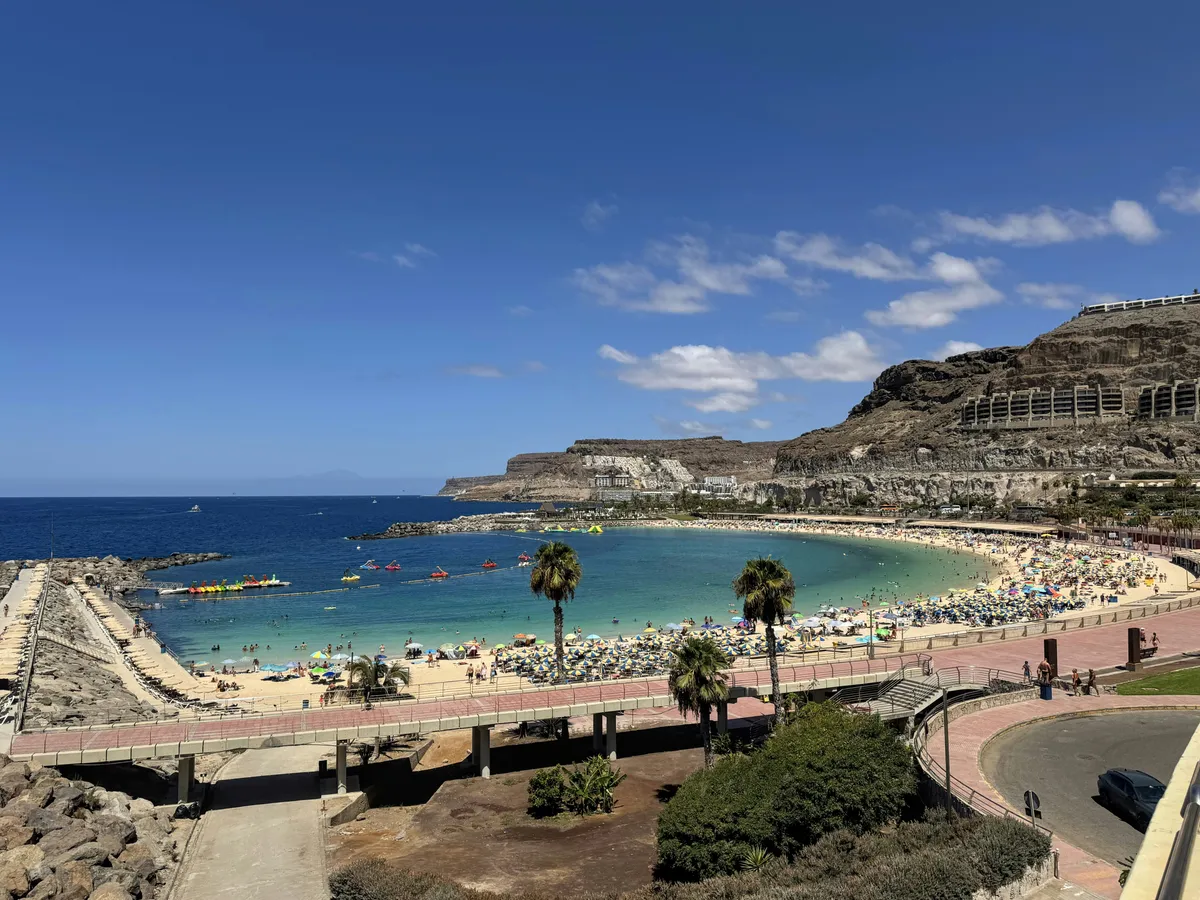 Vista de la playa de Amadores, en forma de media luna, con aguas turquesa, palmeras y acantilados