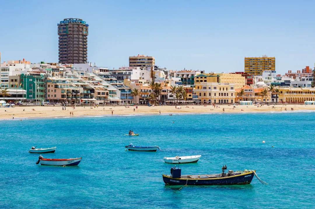 Barcas en el agua turquesa frente a una playa urbana de Las Palmas de Gran Canaria